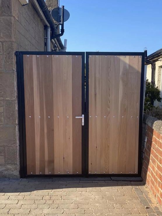 Double gate clad in cedar boards set into a black steel frame