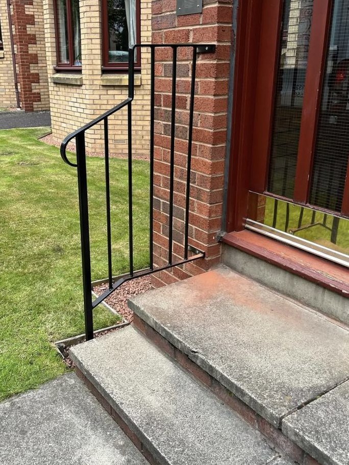 Curved black handrail fitted at the entrance steps of a sheltered housing block