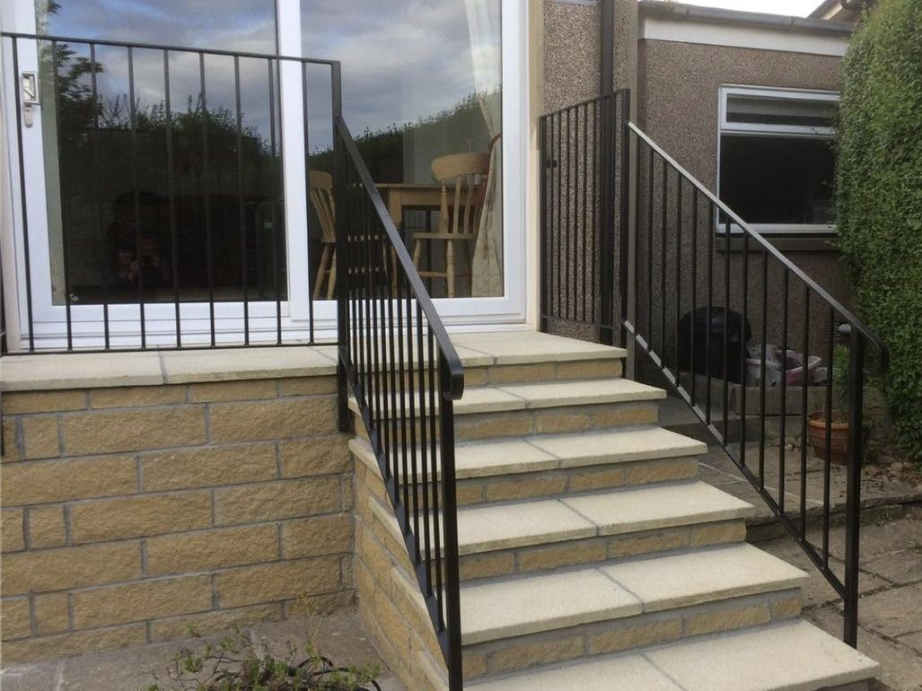 Black handrail following a flight of stone garden steps up to a patio door